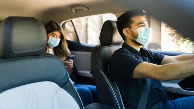 Photo of a man driving a car with a passenger in the back