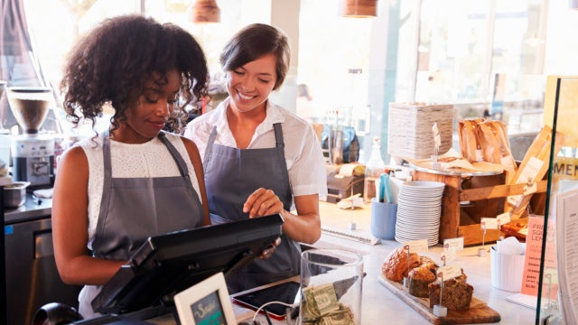 Photo of two smiling women working behind the counter of a delicatessen